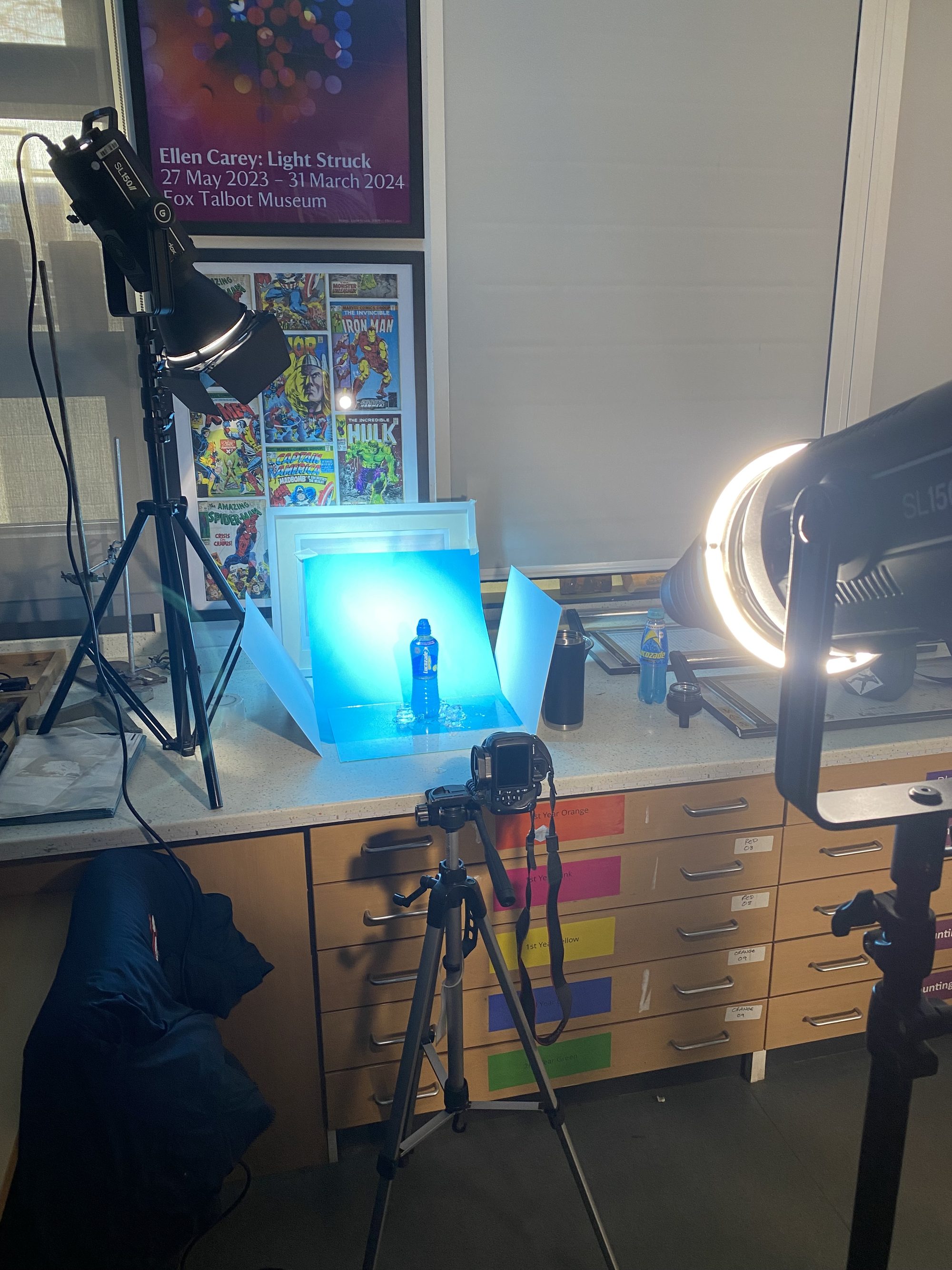 Studio set up — wider view of the lighting rig, comic-poster wall, and tripod-mounted camera